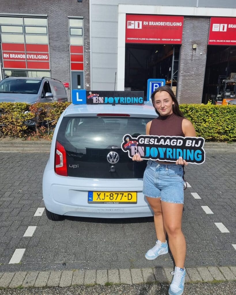 Geslaagde leerling van rijschool EnjoyRiding poseert met certificaat bij lesauto na rijexamen Geslaagde leerling van rijschool EnjoyRiding poseert met certificaat bij lesauto na rijexamen
