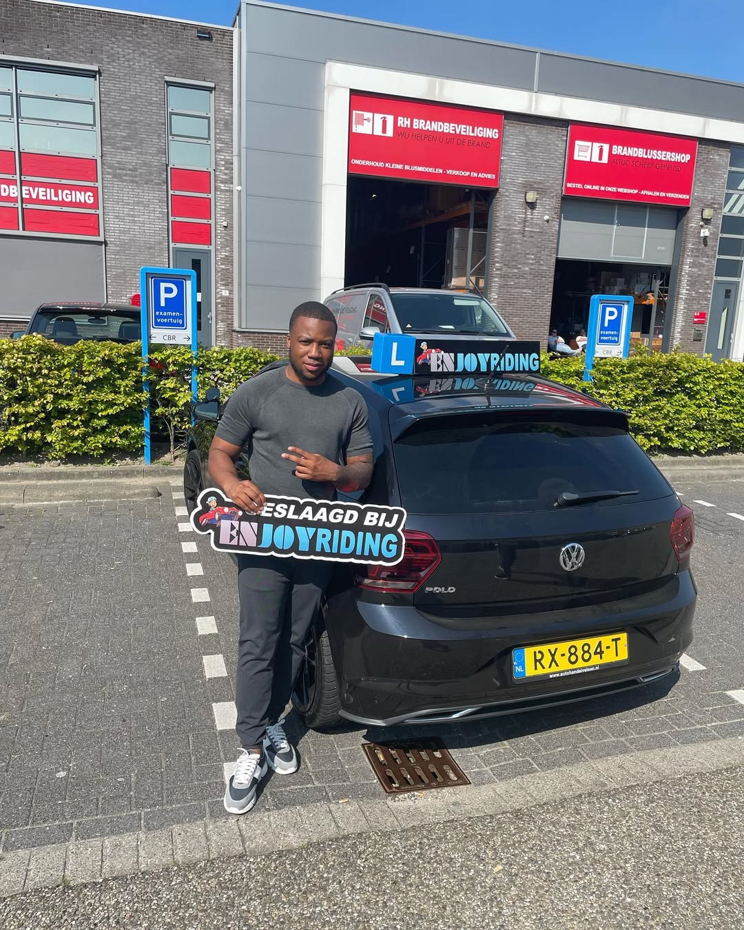 Geslaagde student van Rijschool EnjoyRiding poseert met rijbewijs en auto na het behalen van rijexamen